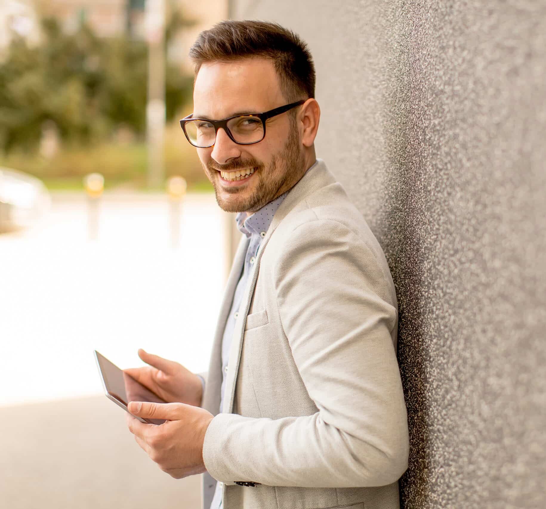 Handsome,Young,Businessman,With,Digital,Tablet,By,The,Grey,Wall