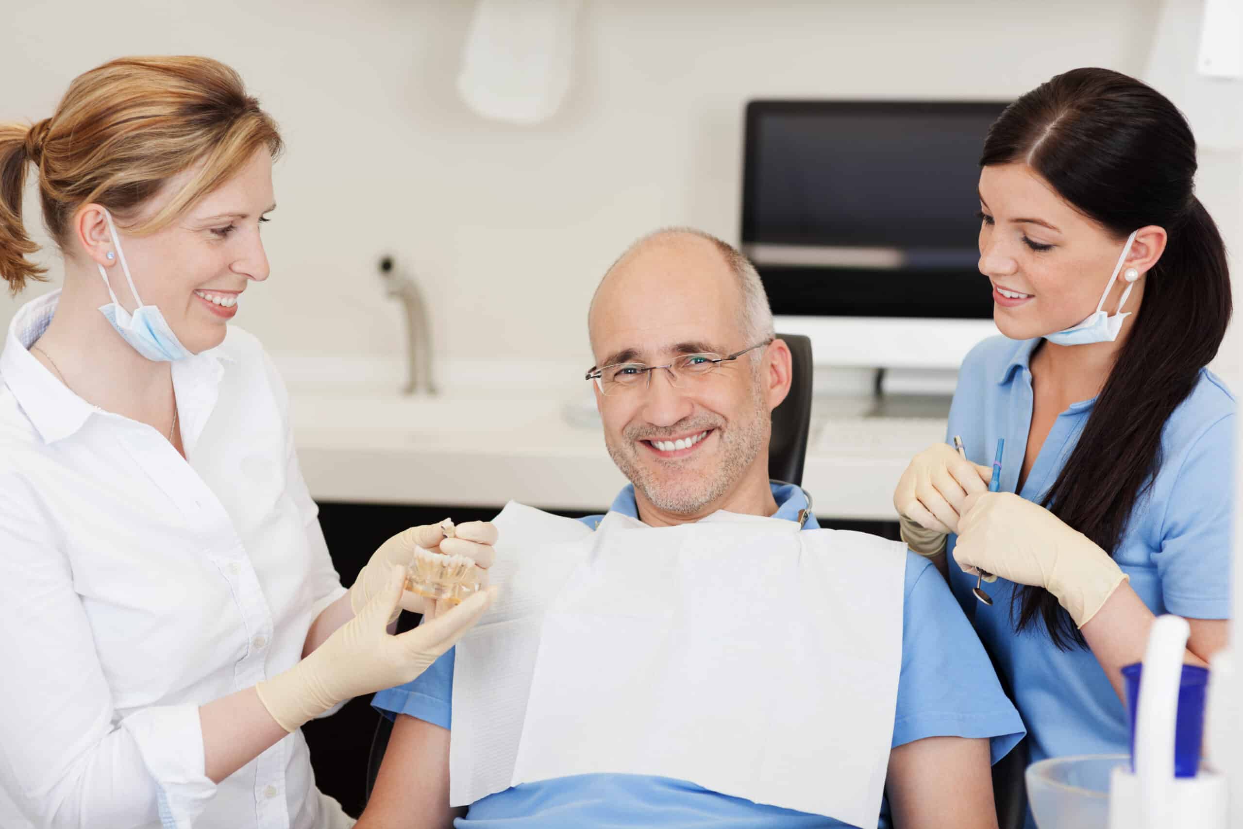Dentist,Explaining,Teeth,Model,To,Smiling,Male,Patient,At,Clinic