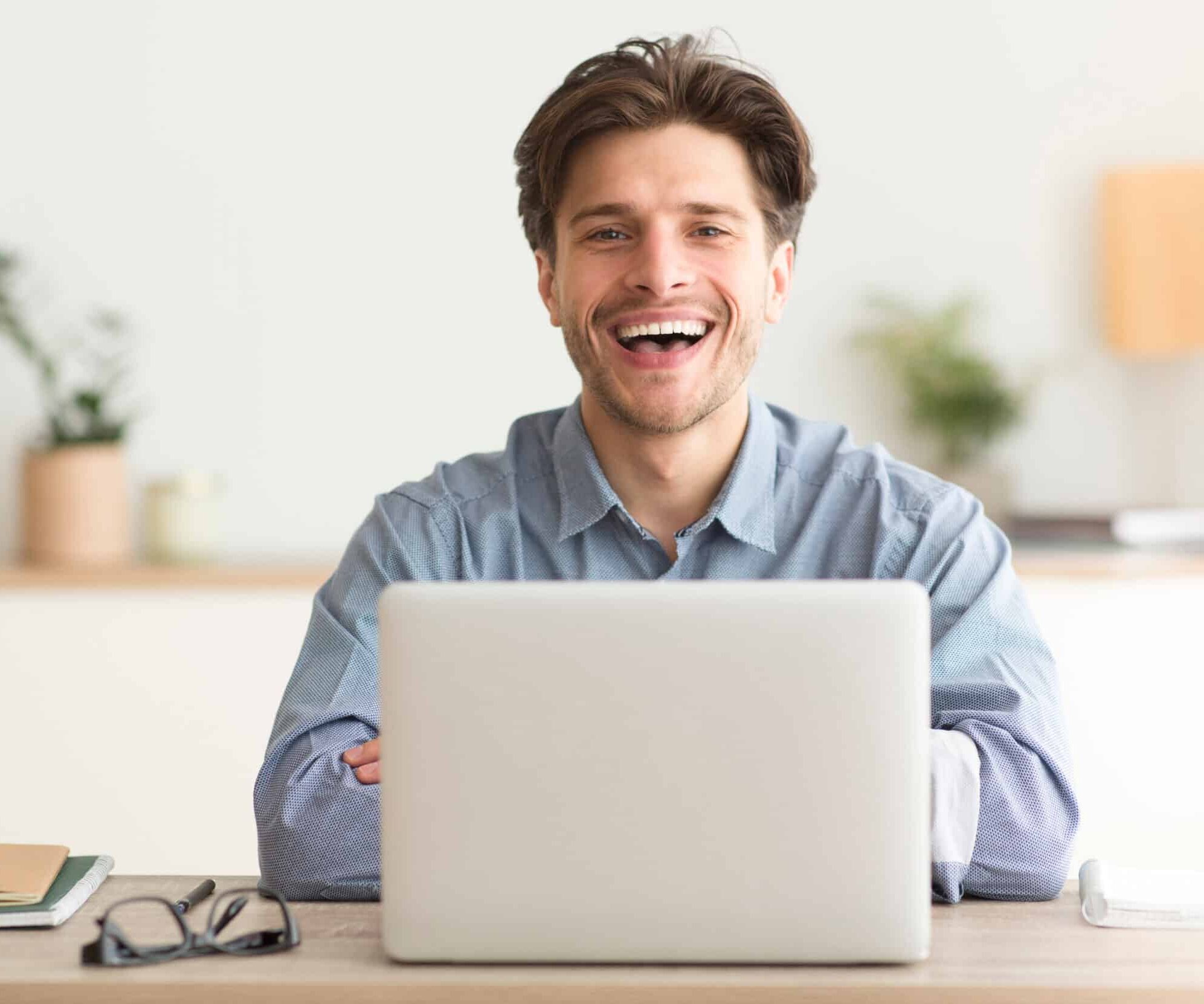 Man,Sitting,At,Laptop,And,Laughing,Looking,At,Camera,Indoor.
